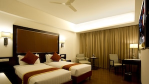 A hotel room with two beds, a desk, a chair, a TV, and a ceiling fan. - Jubilee Ridge (Hyderabad)