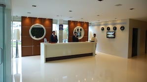 A hotel reception area with a modern design, featuring a reception desk, a large mirror, and a wall-mounted TV displaying a cityscape. - Jubilee Ridge (Hyderabad)