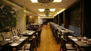 A long dining area with multiple tables set for service, a large plant on the left, and a patterned wall on the right. - Jubilee Ridge (Hyderabad)