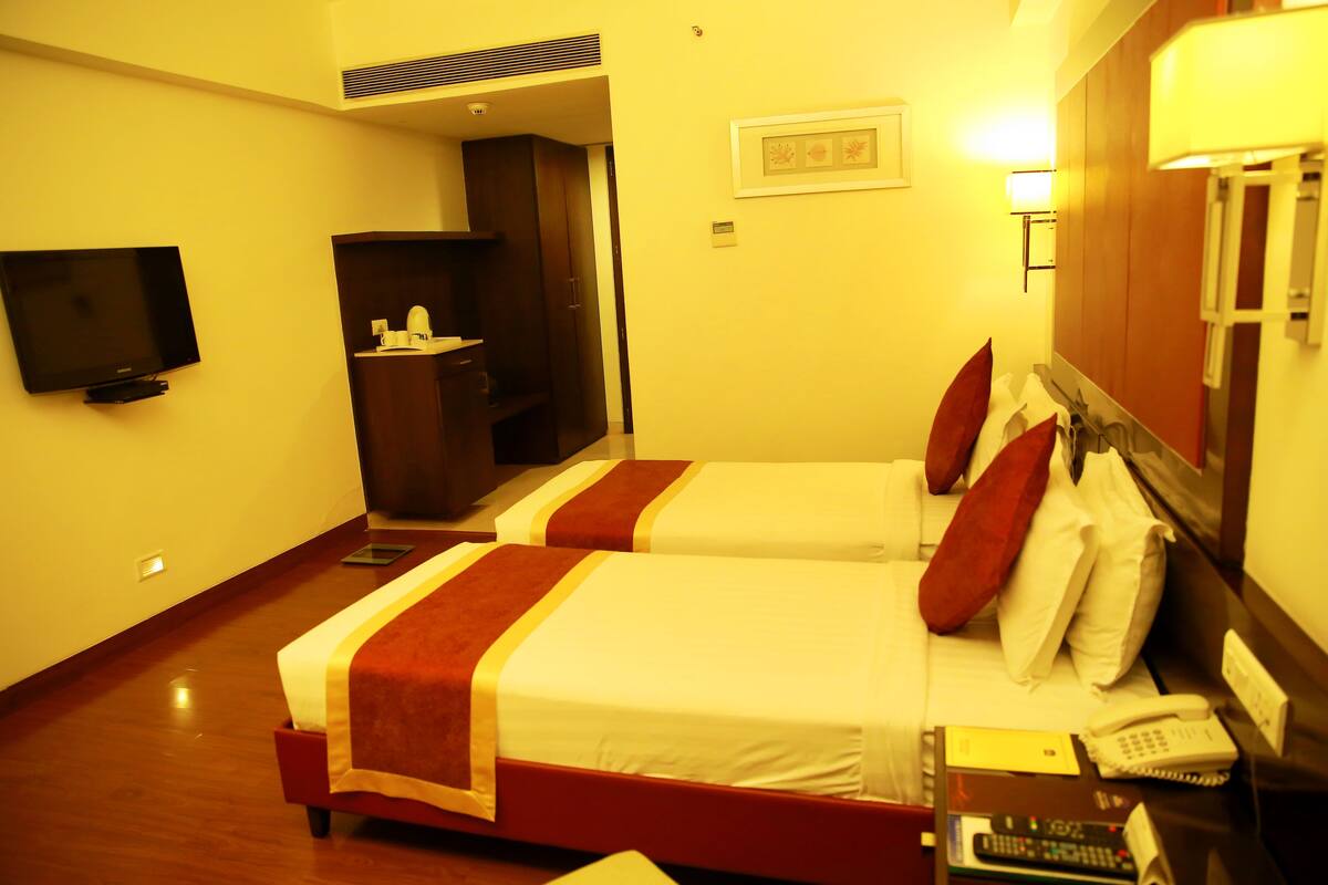 A hotel room with two beds, a television, a desk with a telephone, and a mirror.