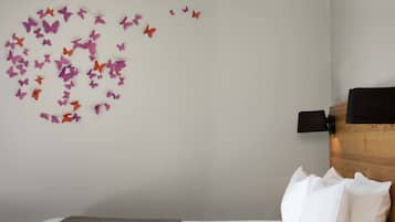 Un dormitorio con cama, almohadas blancas, cabecero de madera, lámpara de pared y decoración de mariposas en la pared.