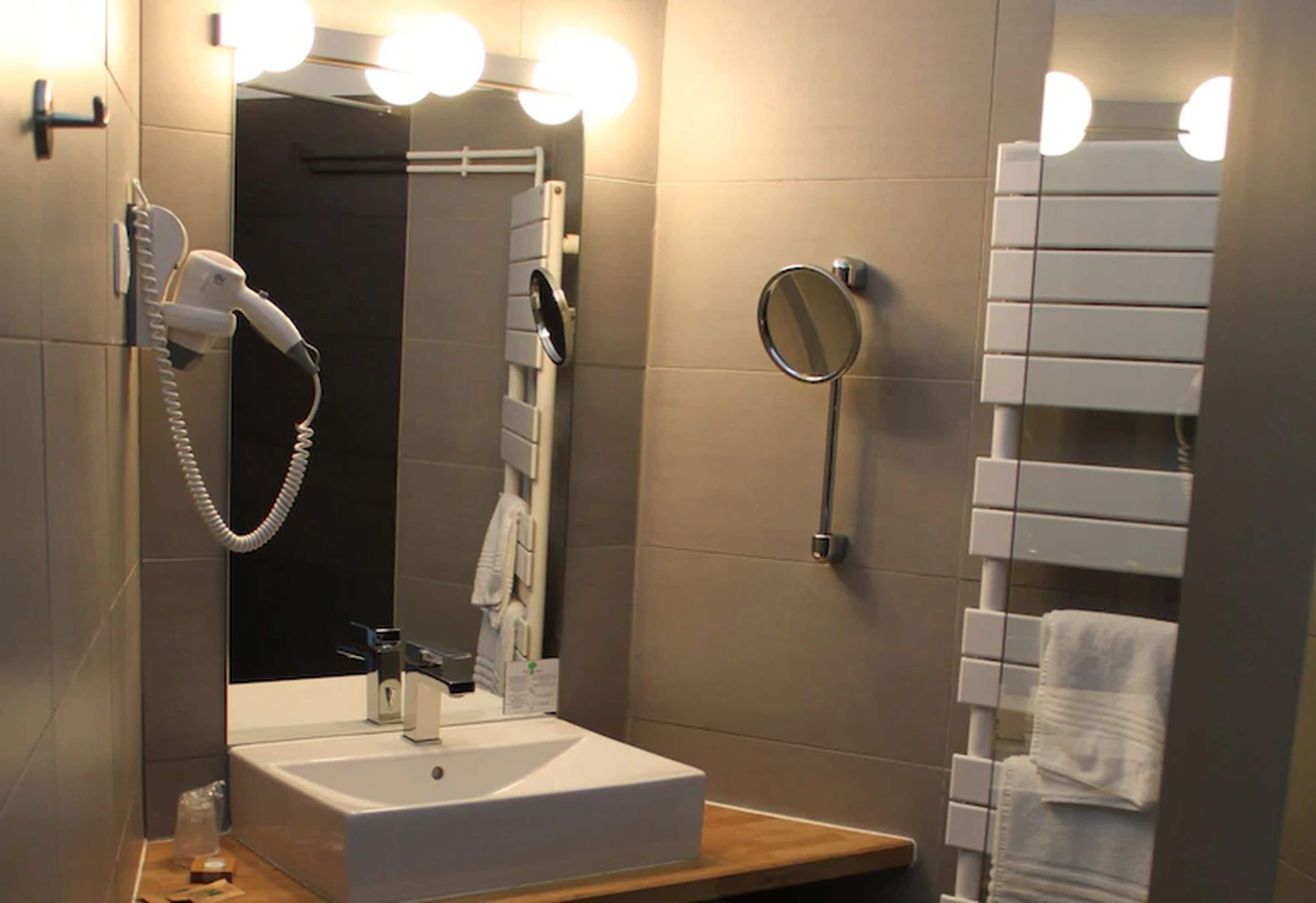 A modern bathroom with a white sink, a hairdryer, a mirror, and a towel rack.