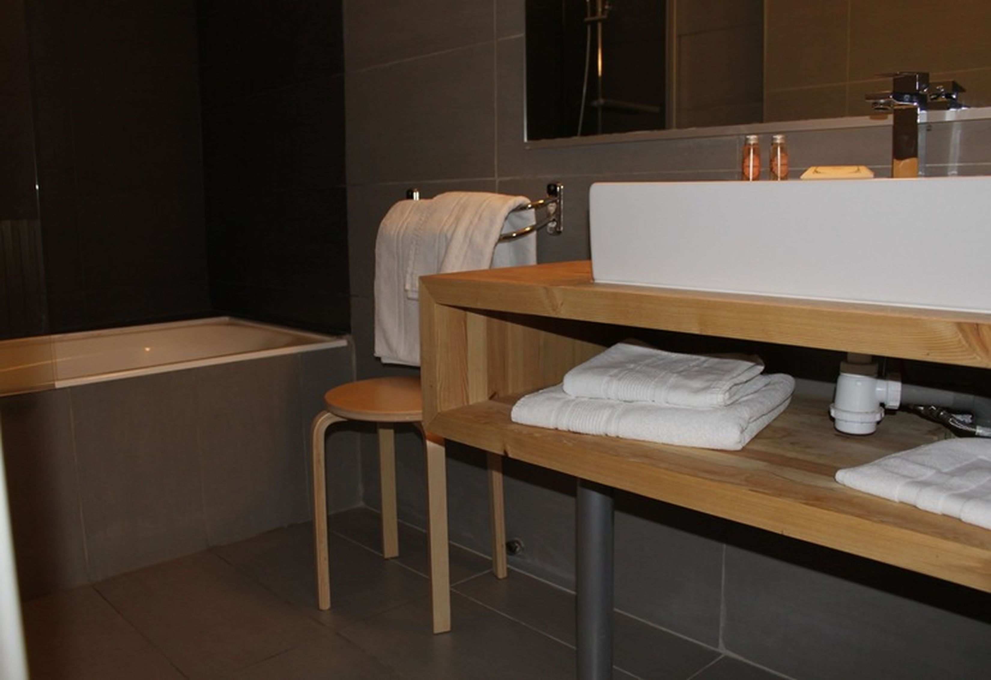 A modern bathroom with a wooden vanity, a bathtub, and a large mirror above the sink.