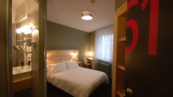 Habitación de hotel con cama, mesita de noche, lámpara, espejo y el número 51 en la puerta.