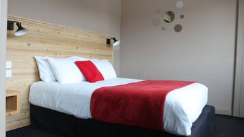 Cama bem arrumada com roupa de cama branca e vermelha, cabeceira de madeira e mesa de cabeceira pequena.