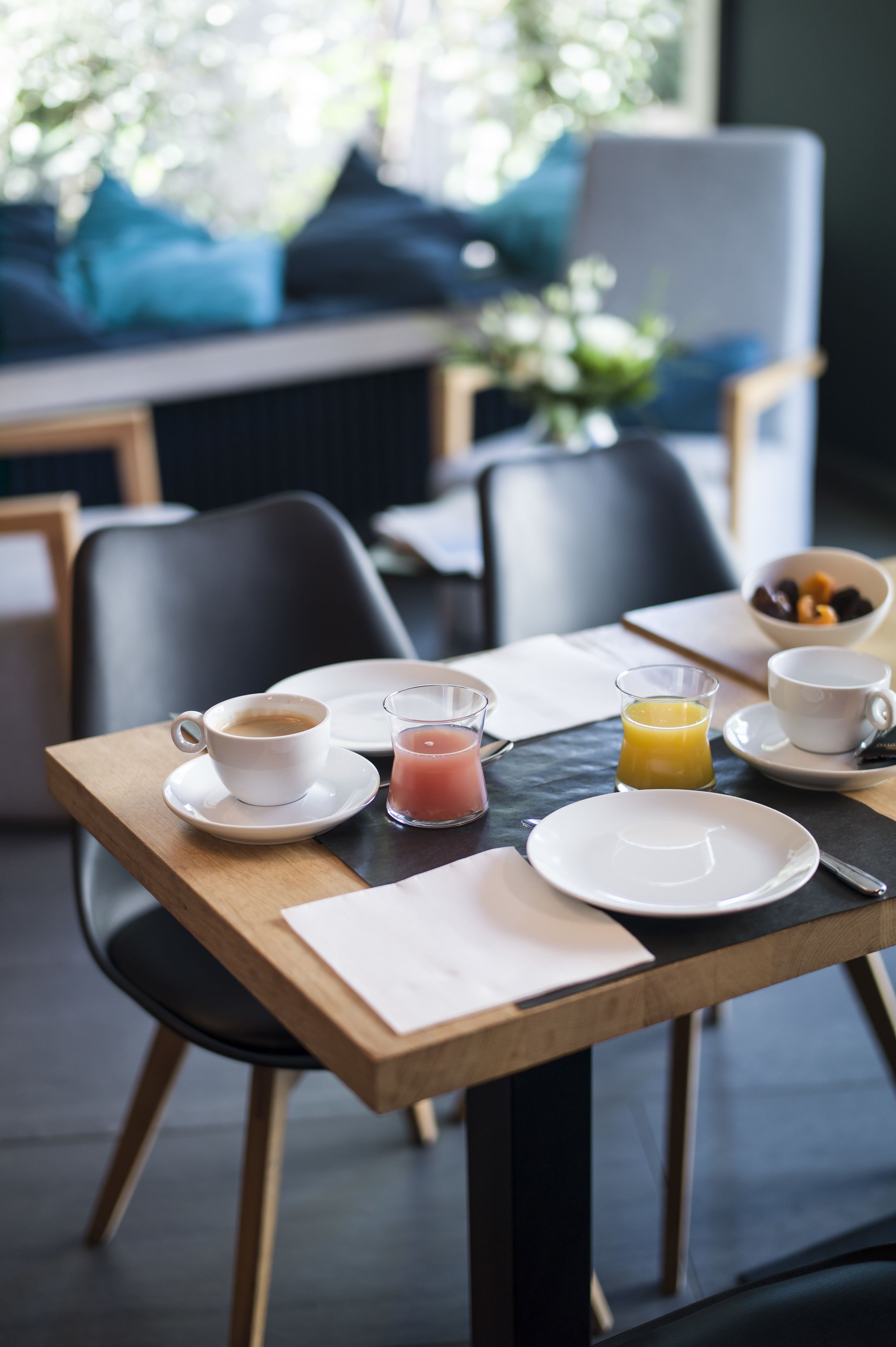 A breakfast table with a cup of coffee, a glass of orange juice, and a bowl of fruit.