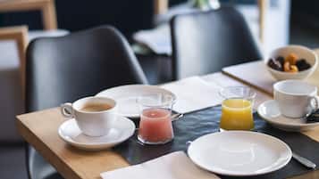 A breakfast table with a cup of coffee, a glass of orange juice, and a bowl of fruit.