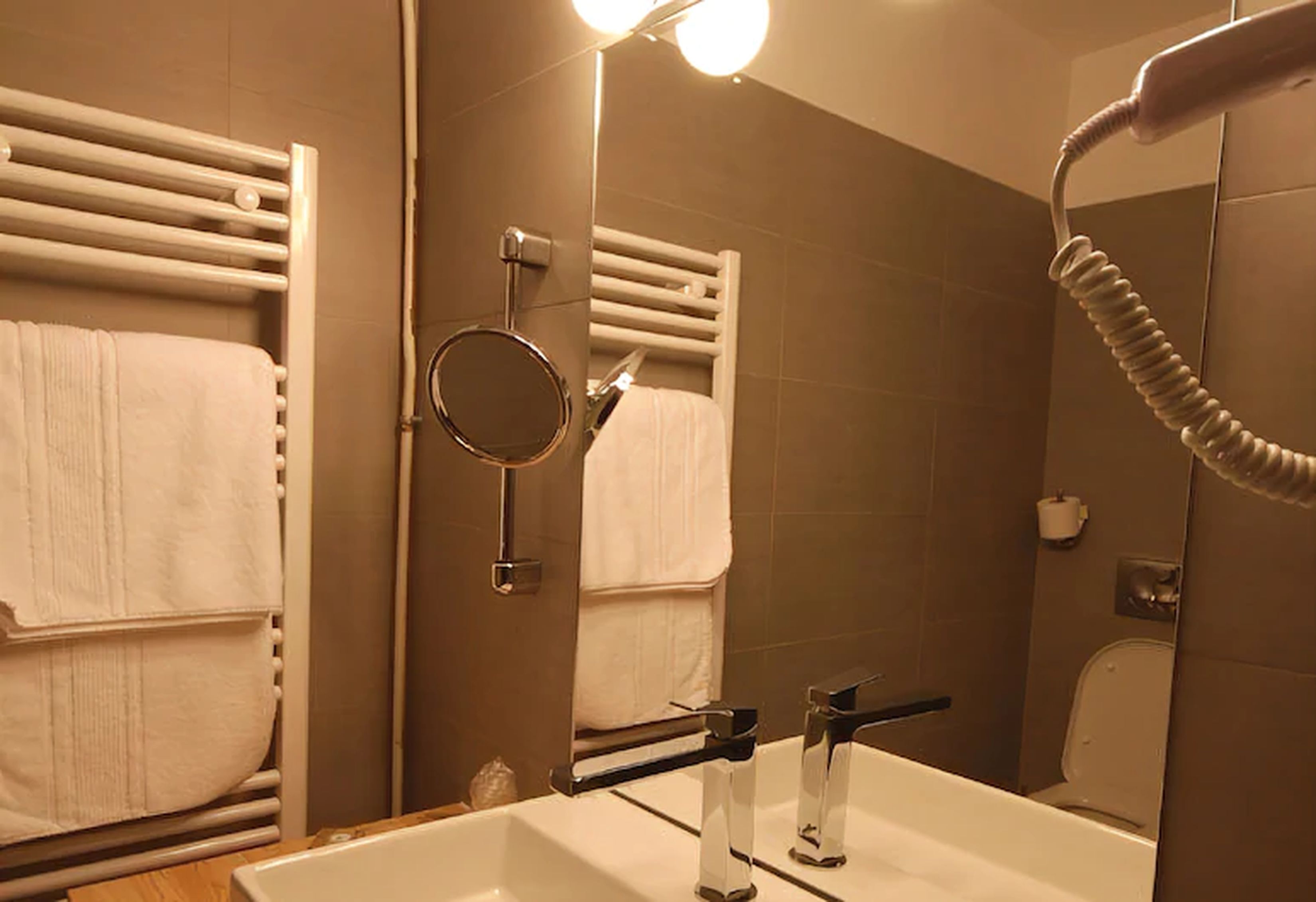 Un baño con lavamanos blanco, un espejo, un perchero para toallas y un secador de pelo.