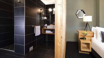 Un baño moderno con ducha, lavamanos y una mesita de noche de madera con lámpara.
