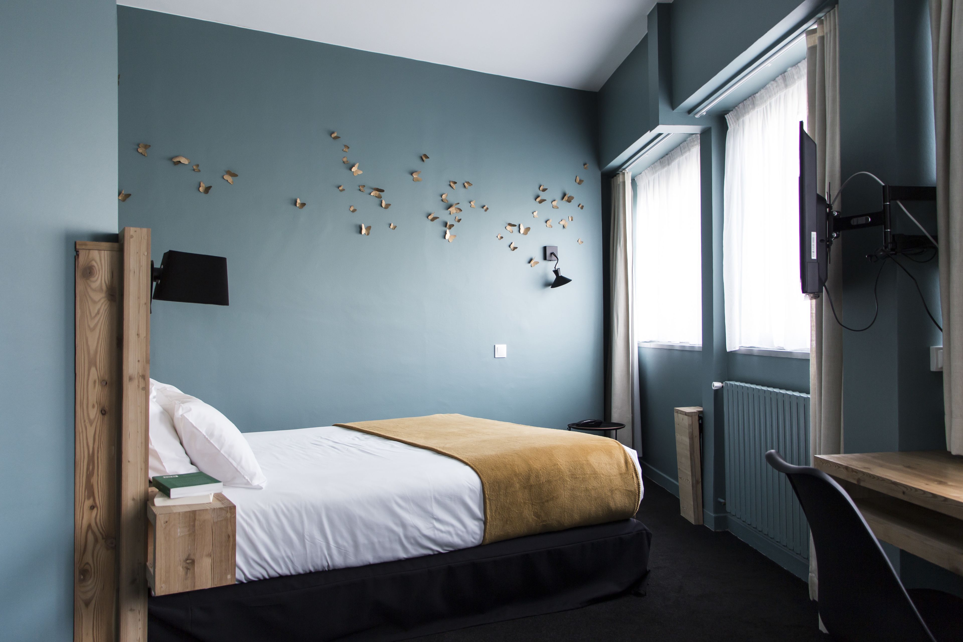 Ein Schlafzimmer mit Bett, Nachttisch, Lampe und einer Wand mit Schmetterlingsdekorationen.