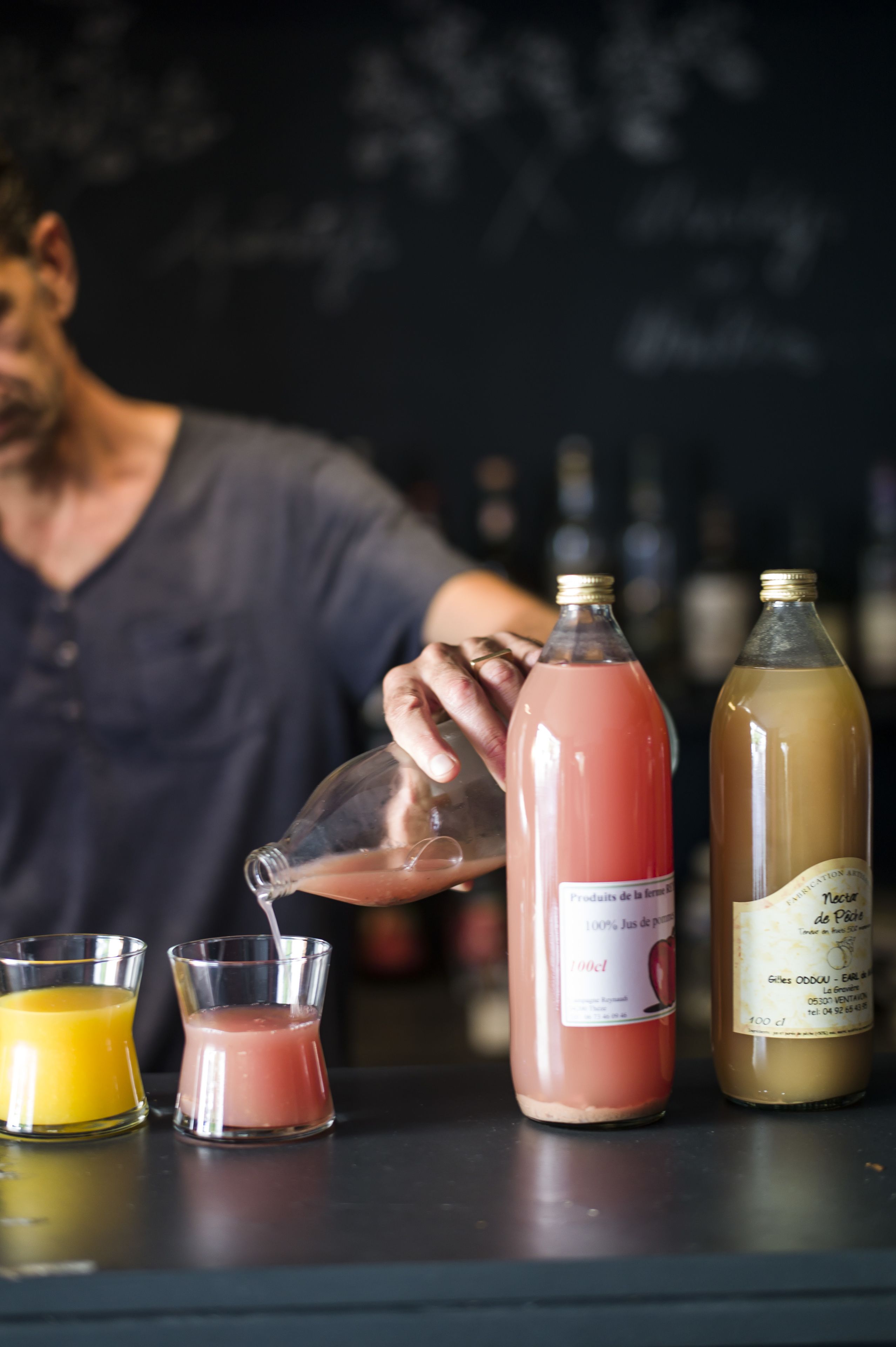 A bar setting with a person pouring a drink into a glass. There are two bottles and two glasses on the counter.