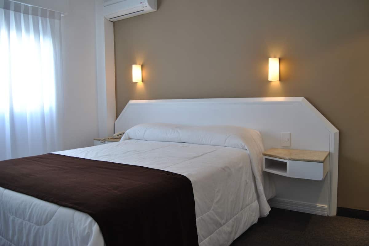 Habitación de hotel con una cama, una mesita de noche, un estante montado en la pared y dos apliques.