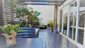 Eine Terrasse im Freien mit Tisch und Stühlen, umgeben von Blumentöpfen und einer Pergola.