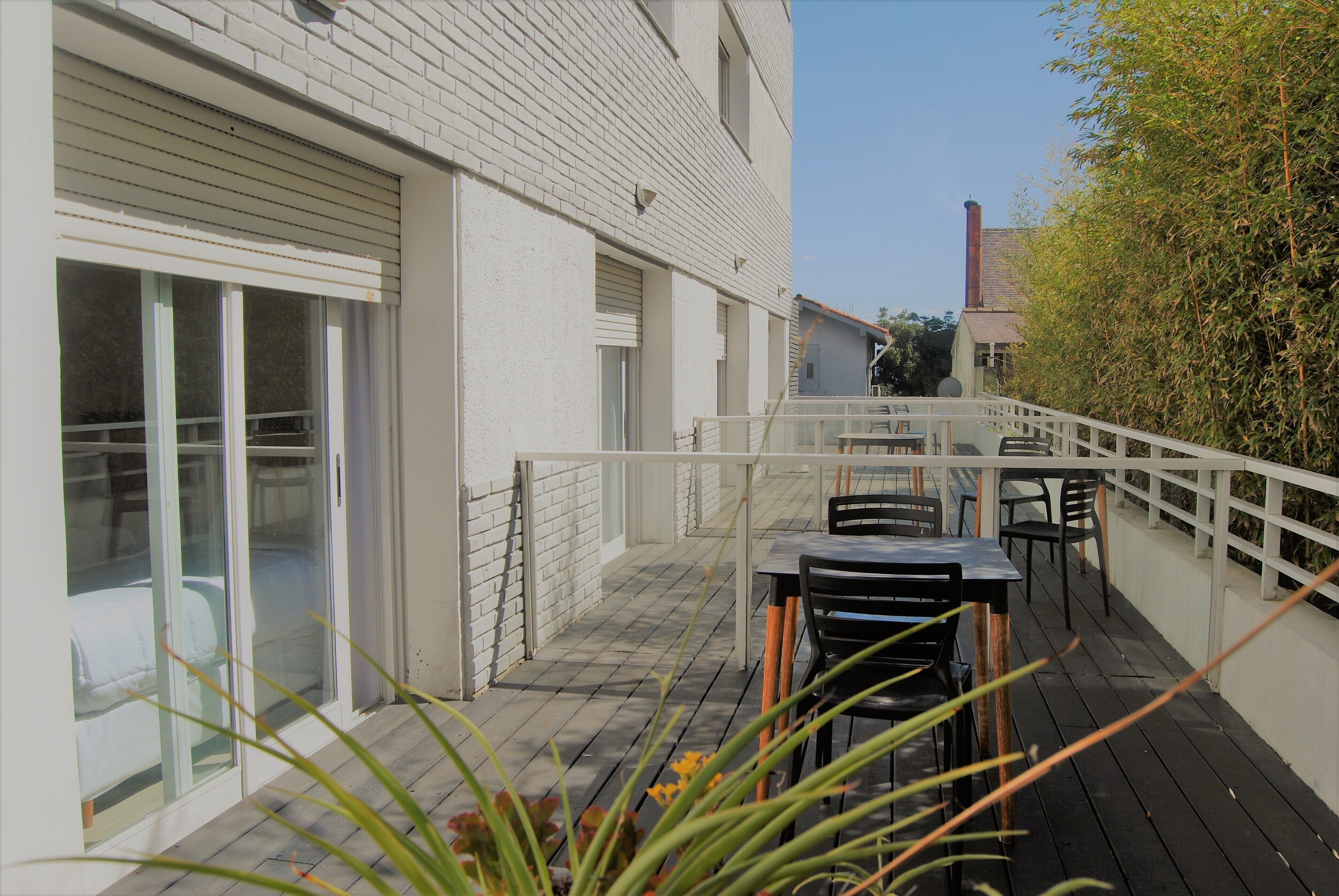 A balcony with a table and chairs, a sliding glass door, and a view of a building with a chimney.