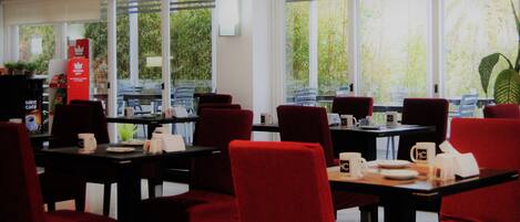 Un restaurante con sillas y mesas rojas, ventanas amplias y vistas a zonas verdes.