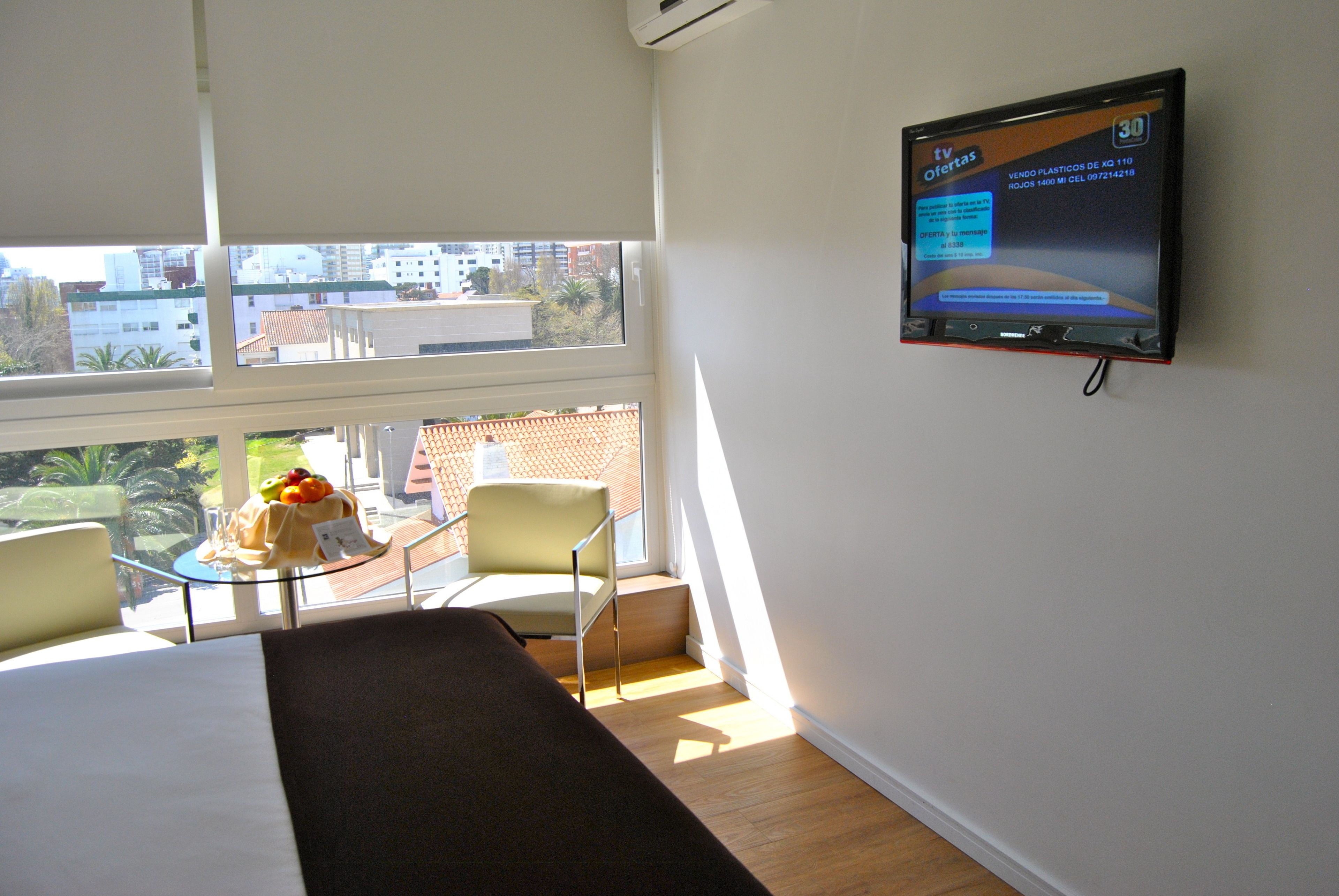Habitación de hotel con una cama, un televisor montado en la pared, una mesita con frutero y una silla.