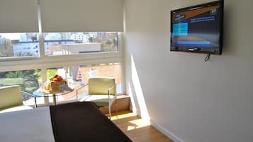 Habitación de hotel con una cama, un televisor montado en la pared, una mesita con frutero y una silla.