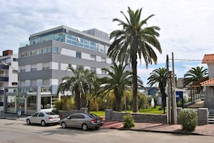 A modern hotel with a glass facade, palm trees, and a parking lot.