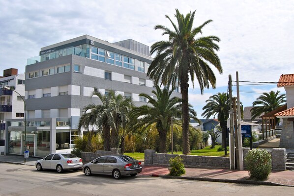Un hotel moderno con fachada de vidrio, palmeras y estacionamiento.