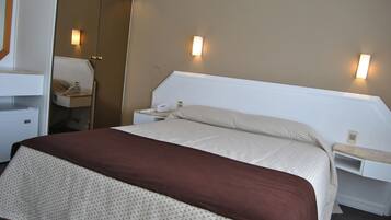 Une chambre d’hôtel bien aménagée, avec un grand lit, des tables de chevet, un miroir et deux lampes fixées au mur.