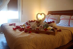 Una cama con una toalla dispuesta en forma de corazón, pétalos de rosa y una bandeja con alimentos para el desayuno.