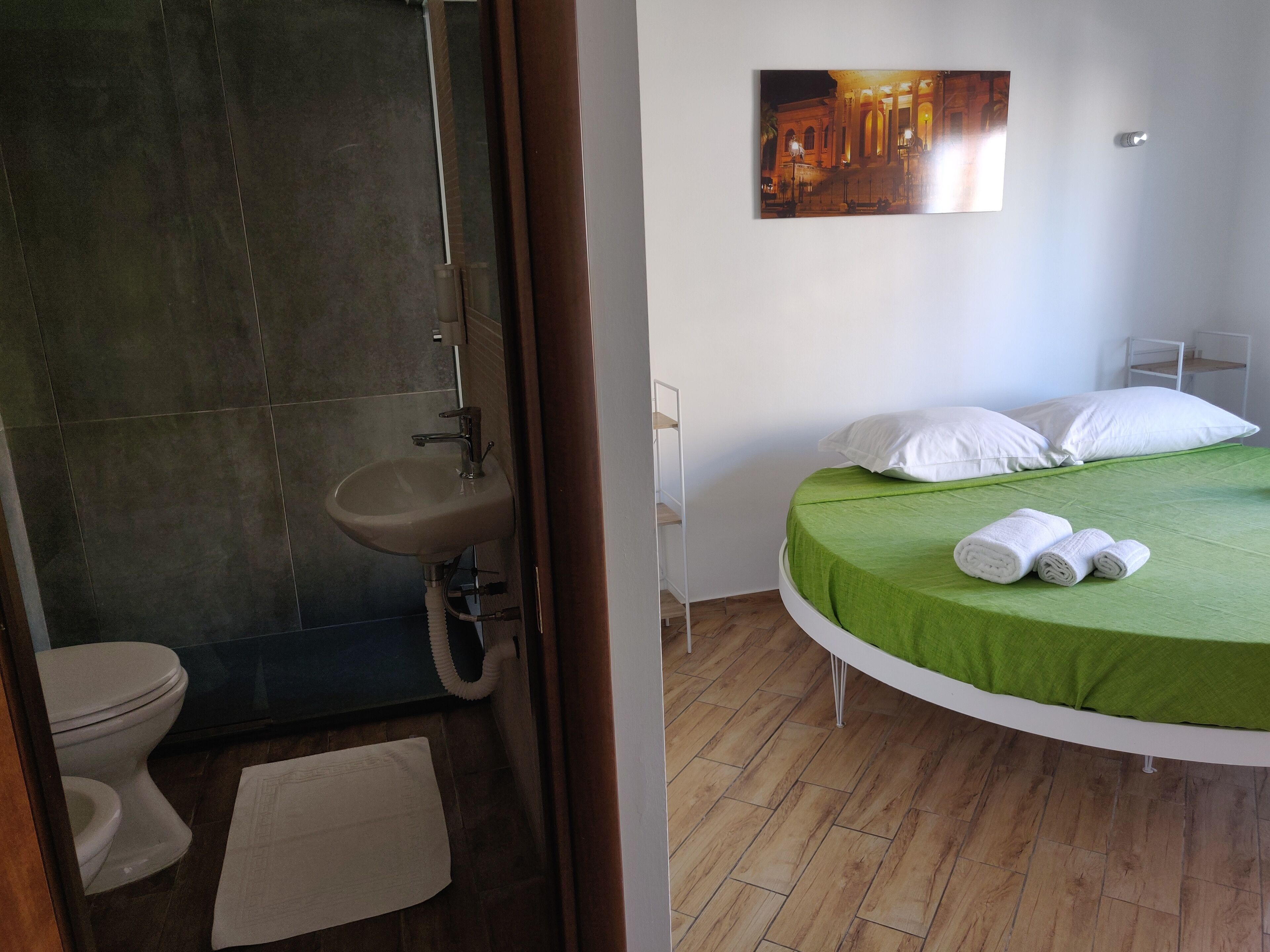 Ein Badezimmer mit Waschbecken, Toilette und Dusche. Der Raum verfügt über ein Bett mit grüner Bettwäsche und weißen Kissen.