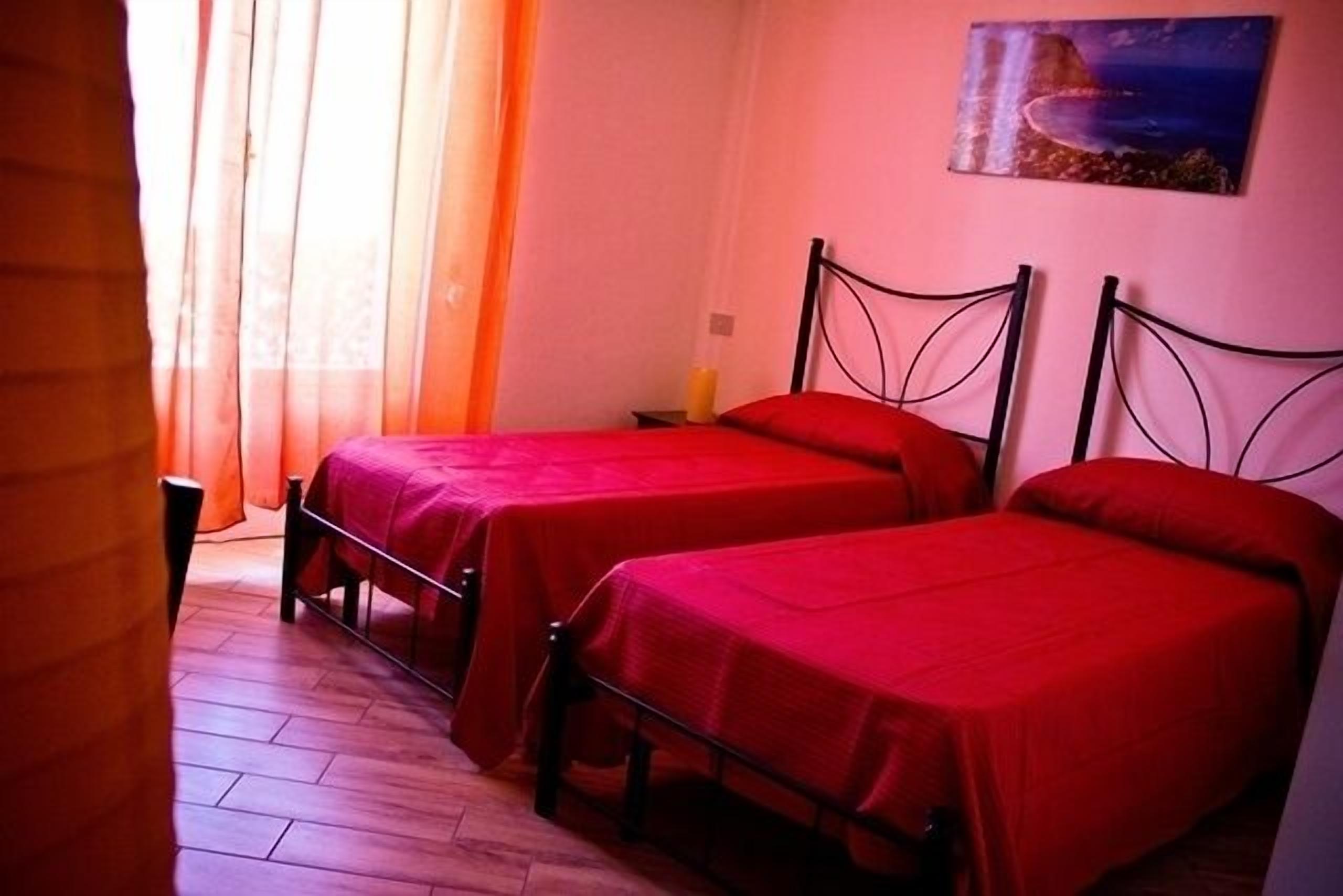 Una habitación con dos camas individuales, piso de madera, un cuadro en la pared y una ventana con cortinas.