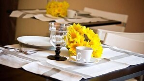 Una mesa de comedor con platos blancos, una copa de vidrio transparente, una taza blanca y un ramo de flores amarillas.