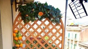 Un pequeño balcón con una silla blanca, un panel de celosía de madera y un taburete morado.