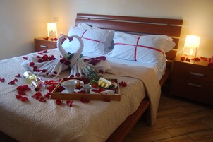 Un lit avec une serviette en forme de cœur, des pétales de rose, un plateau avec de la nourriture et une bouteille.