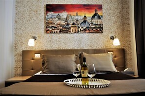 A hotel room with a large bed, two wall sconces, a painting of a cityscape, and a tray with wine glasses and a bottle. - Castel Sant'Angelo Inn (Rome)