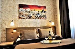 A hotel room with a bed, a nightstand, a tray with a bottle and glasses, and a cityscape painting on the wall. - Castel Sant'Angelo Inn (Rome)