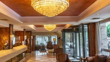 Eine Hotelhalle mit einer großen Kronleuchter, Ledersitzmöglichkeiten, einem Empfangstresen und Blick durch große Glastüren.