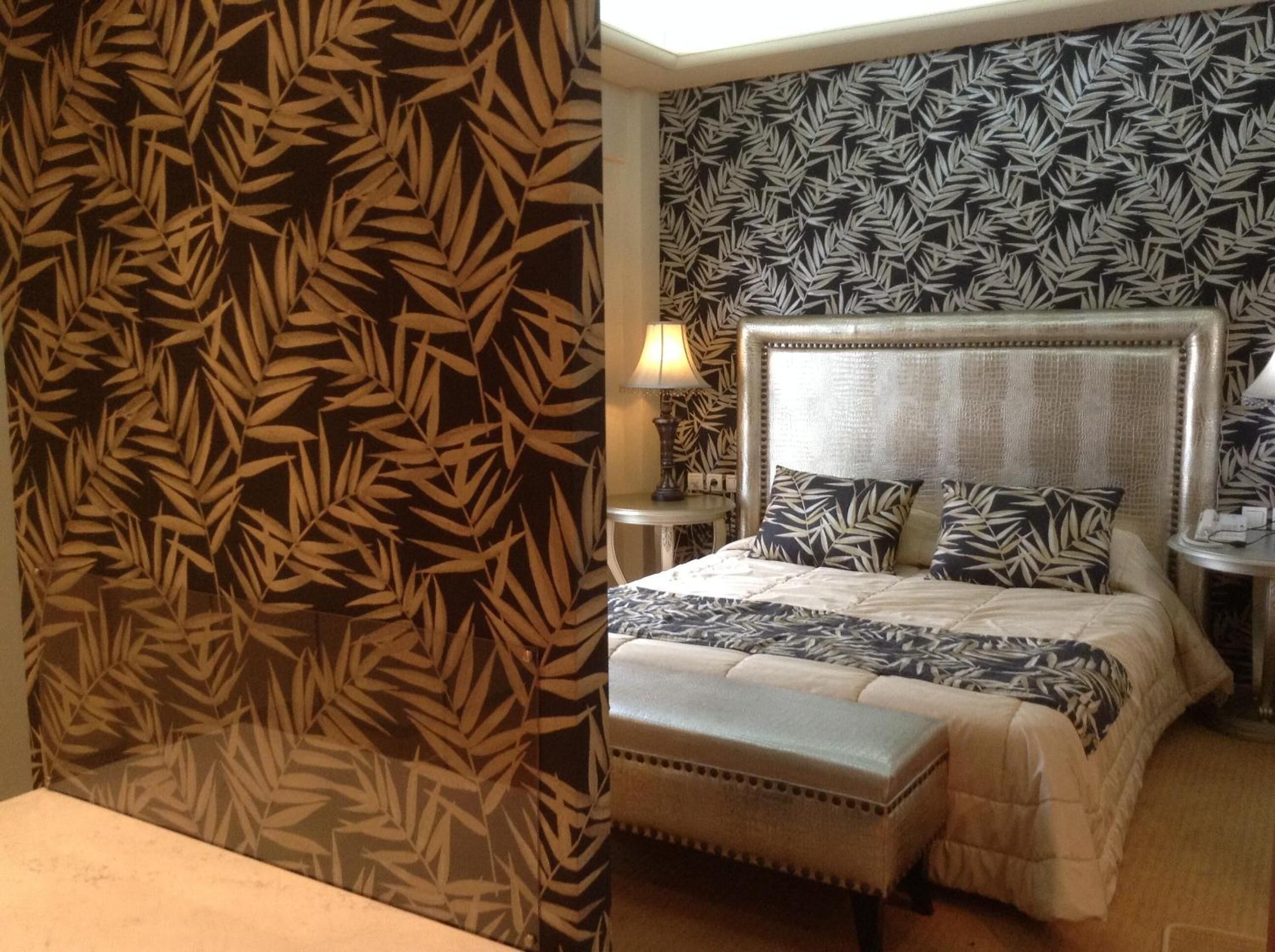 A bedroom with a large bed, a headboard, a bedside table, and a lamp.
