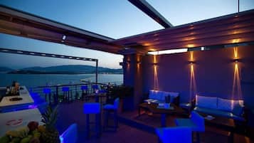 Eine Terrasse mit Sitzgelegenheiten und einem Tisch mit Blick auf ein Gewässer und Hügel.