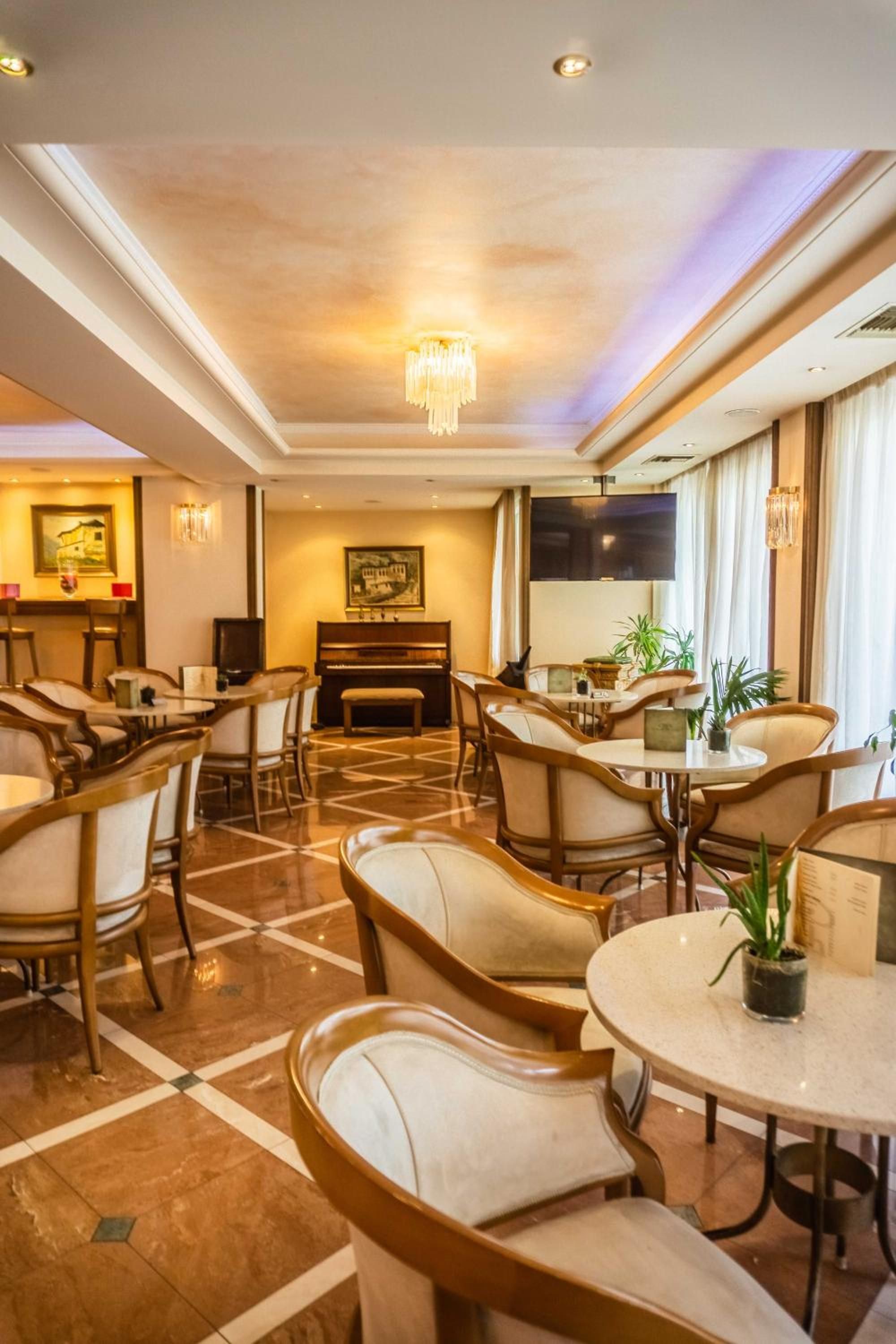 Eine Hotelhalle mit runden Tischen und Stühlen, einem Klavier und einem großen Gemälde an der Wand.