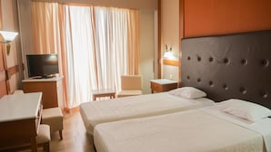 Hotellihuone, jossa on kaksi sänkyä, työpöytä, tuoli, televisio ja lamppu.