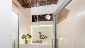 A reception area with a glass partition, a desk with a laptop, and a vase with flowers. - First Floor (Rome)