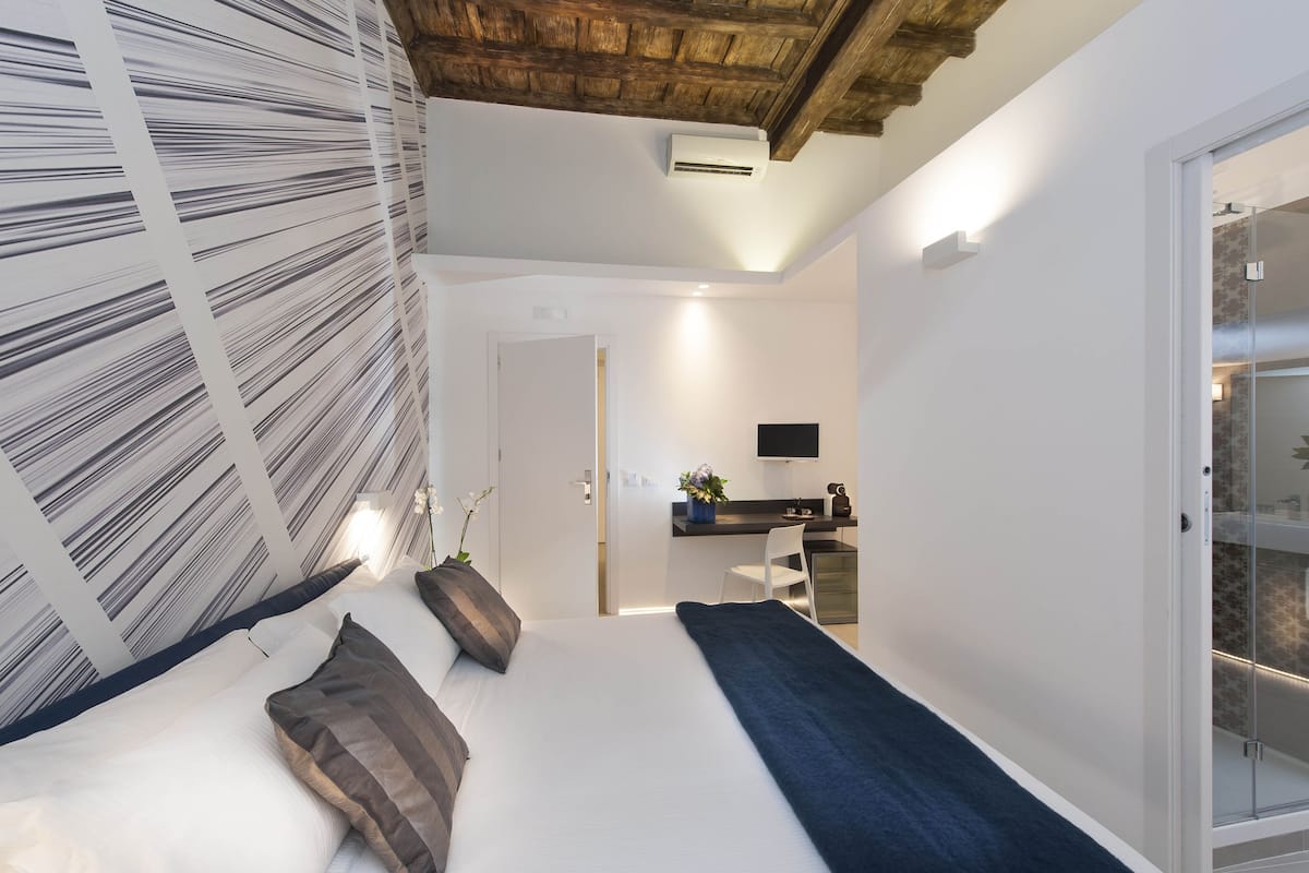 A modern bedroom with a bed, a desk, and a shower area.