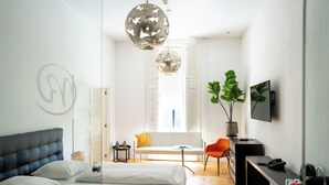 A modern hotel room with a bed, a sofa, a small table, a chair, a TV, and a desk with a telephone.