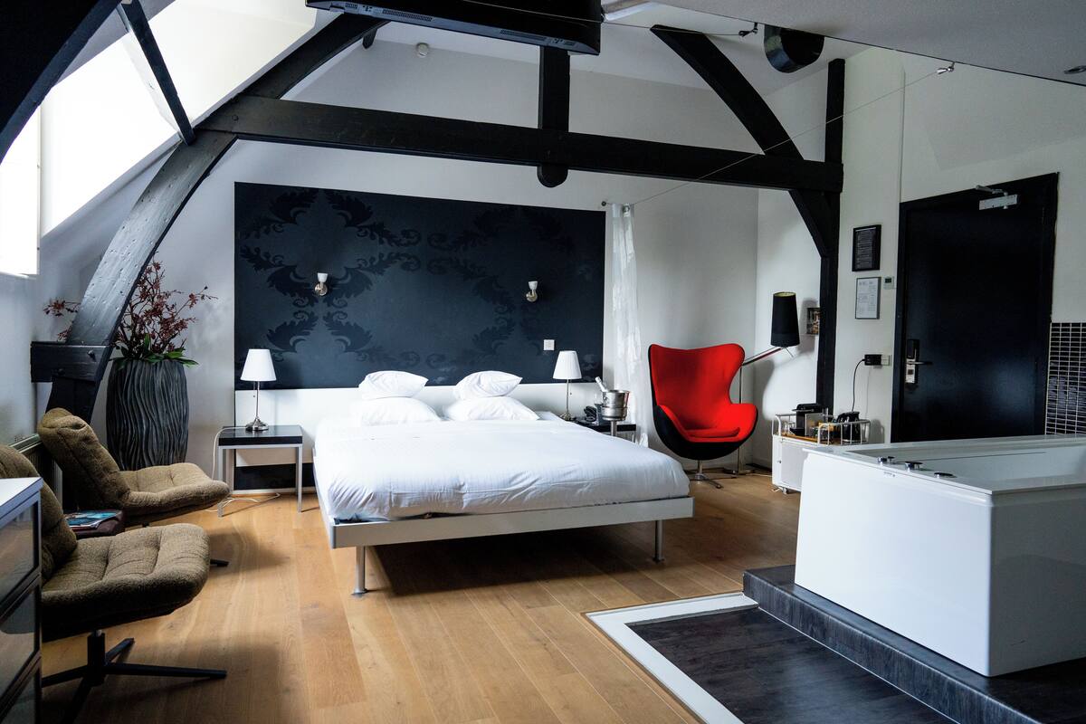 A modern bedroom with a bed, a red chair, a desk, and a large window.