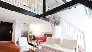A modern interior with a white sofa, a glass coffee table, and a staircase with a black frame.