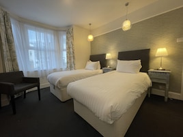 Habitación de hotel con dos camas, una silla y una mesita de noche con lámpara.