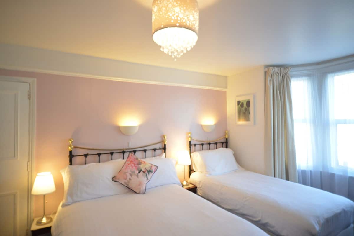 A hotel room with two beds, a chandelier, bedside lamps, and a window with curtains.