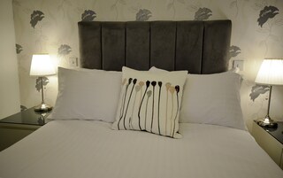 A neatly made bed with a grey upholstered headboard, two bedside lamps, and a floral-patterned wall.
