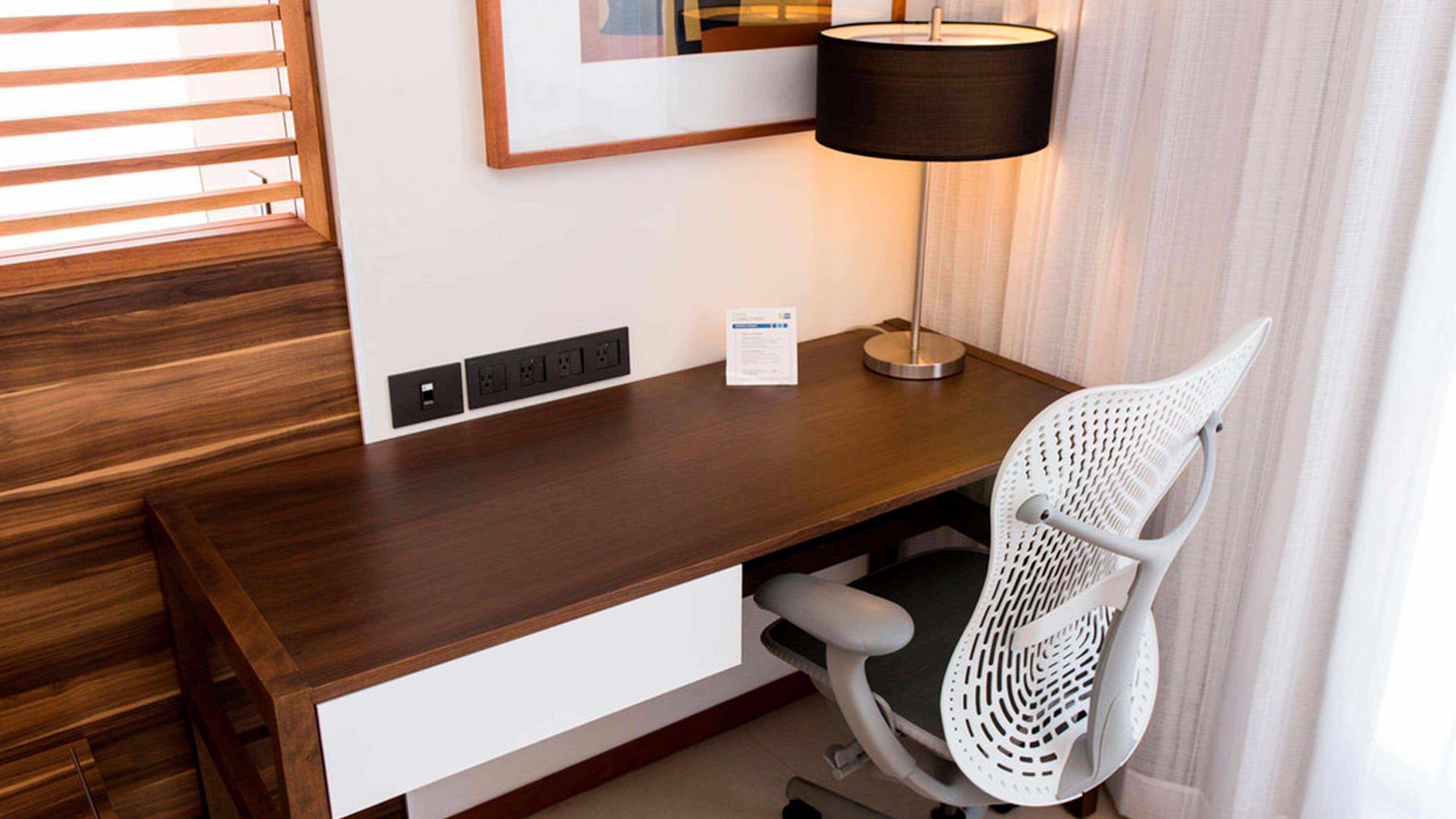 Un bureau en bois, une chaise blanche, une lampe noire et un tableau encadré accroché au mur.
