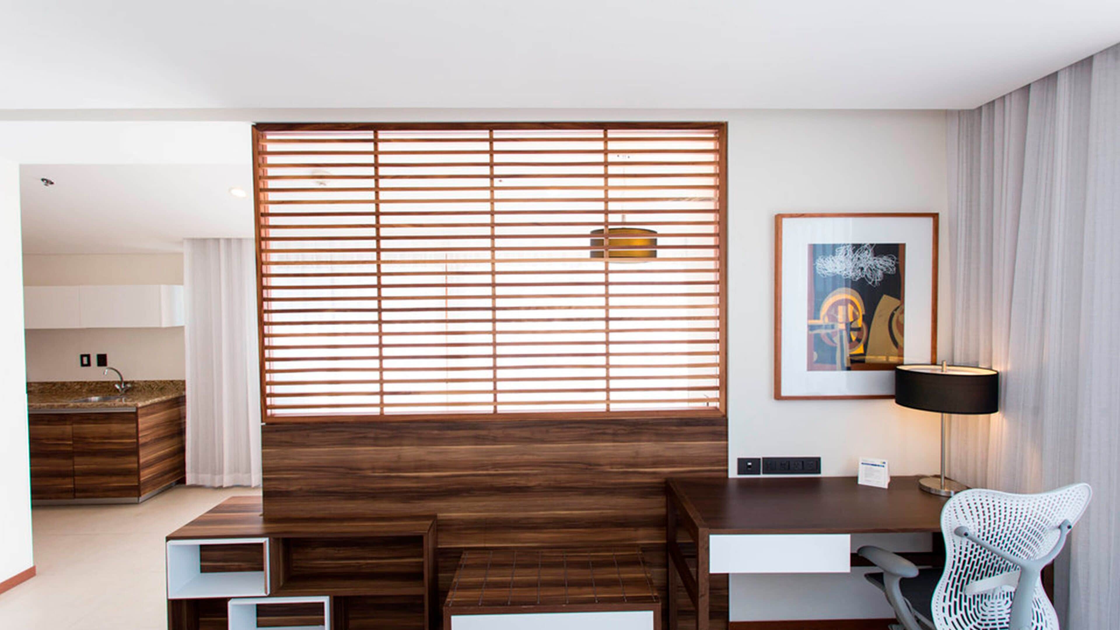Una sala de estar moderna con un separador de madera, un escritorio, una silla y una obra de arte enmarcada en la pared.