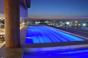 An outdoor swimming pool with a glass barrier, a wooden column, and a view of a cityscape at dusk. - Holiday Inn Express Puerto Vallarta by IHG (Puerto Vallarta)