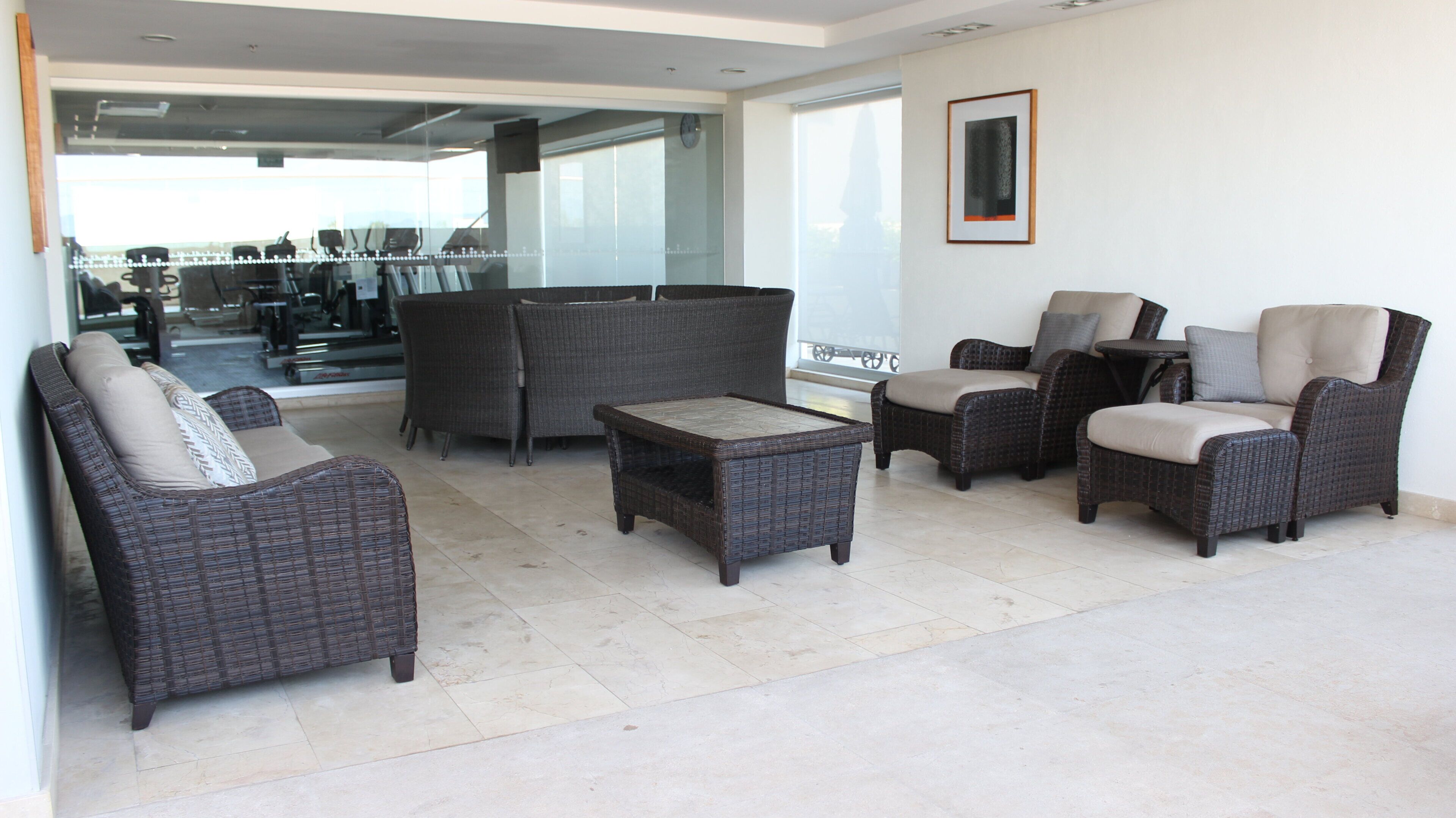 A spacious indoor area with wicker furniture, a glass door leading to a balcony, and a clock on the wall.
