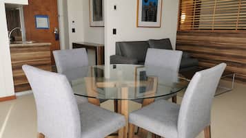 Un salon moderne avec une table basse au plateau en verre, entourée de quatre fauteuils gris à revêtement. Un canapé gris est placé contre le mur, et un panneau décoratif en bois est visible.